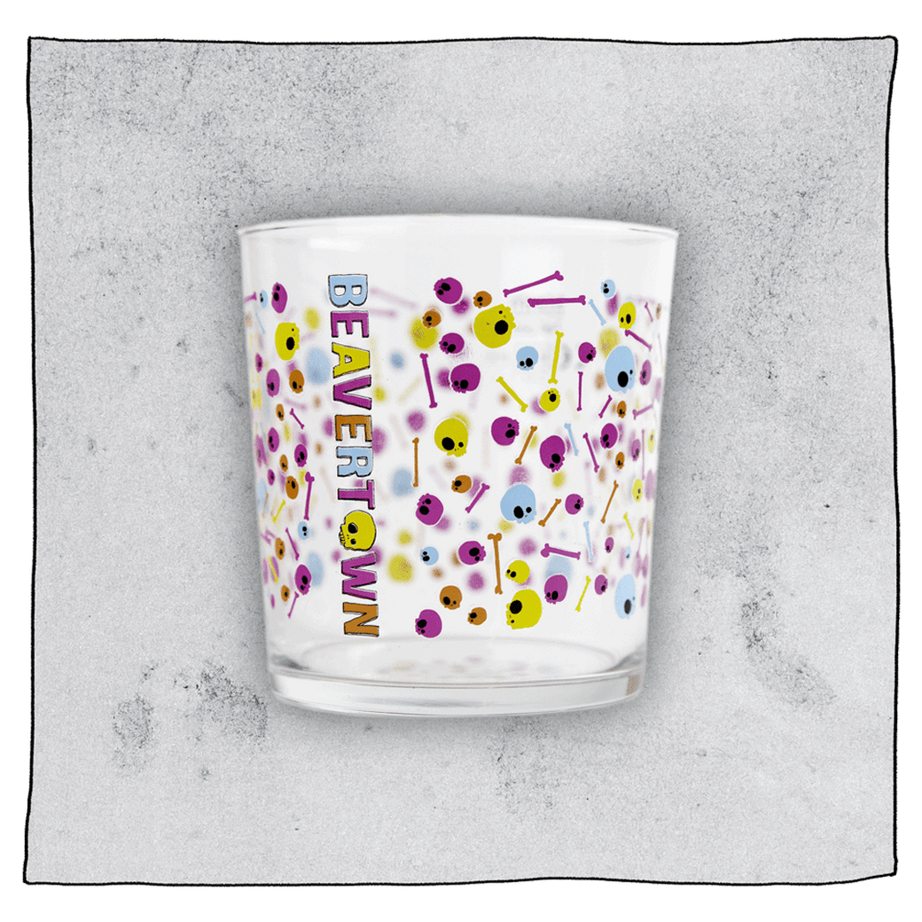 Empty Psychedelic tumbler glass in front of a grey background. Glass is clear with colourful skulls and bones scattered all around the glass.